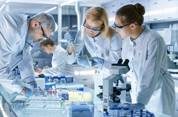 Team of Medical Research Scientists Work on a New Generation Disease Cure. They use Microscope, Test Tubes, Micropipette and Writing Down Analysis Results. Laboratory Looks Busy, Bright and Modern.